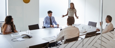 masthead businesswoman giving boardroom presentation viewed through meeting room window